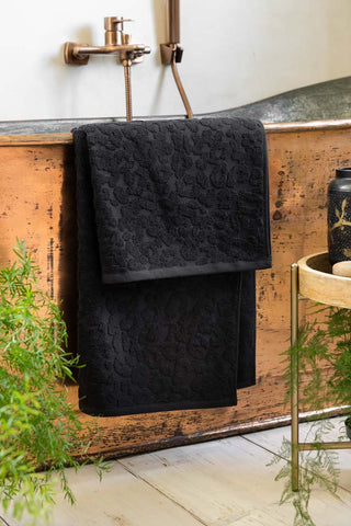 Leopard Jacquard Bath Towels in Jet Black styled against a copper bath tub and white walls. 