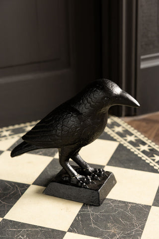 The Black Raven Cast Iron Doorstop on a geometric floor mat in front of a dark wall.