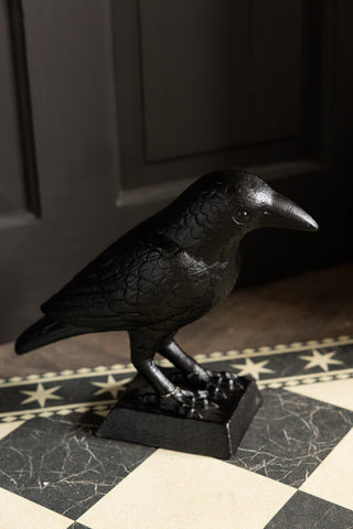 The Black Raven Cast Iron Doorstop styled on a geometric floor mat with a black background.