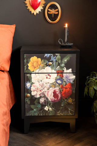 A head on shot of the Black Still Life Floral Bedside Table, styled in a black bedroom with plants and vintage wall art. 