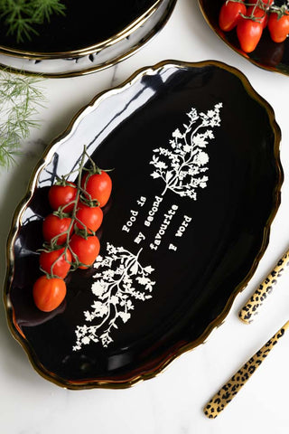 The Black & Gold Floral F Word Serving Platter styled with some vine tomatoes on, displayed as part of a tablescape.