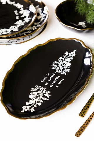 The Black & Gold Floral F Word Serving Platter on a table with some cutlery and other plates.