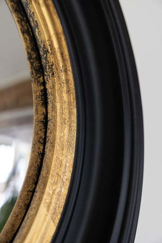 Close up image of black and gold framed convex mirror showing the gold detail