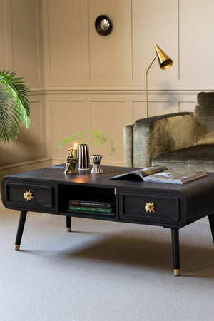 Image of Black & Gold Ringo Storage Coffee Table, shown against a panelled wall, next to a green velvet sofa. 