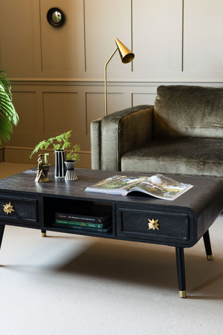 The Black & Gold Ringo Storage Coffee Table shown next to a green velvet sofa. 