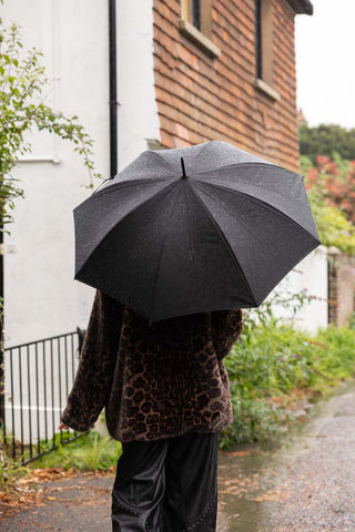 The Black & Leopard Print Umbrella shown from the back with a person walking in the rain.