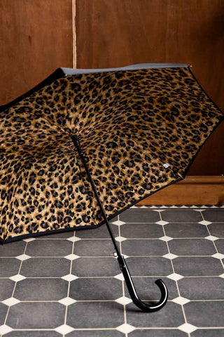 The Black & Leopard Print Umbrella shown inside against a wood wall. 