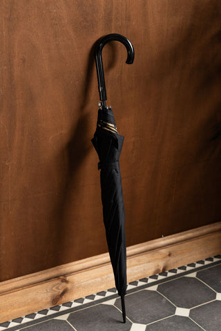The Black & Leopard Print Umbrella shown closed and leaning against a wood wall. 