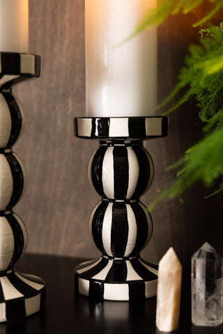 A closer lifestyle image of a black and white striped candle holder against a warm wood background