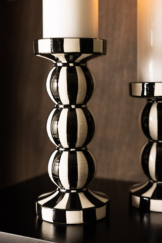 A tall black and white striped candle holder with a candle inside, styled on a dark surface with a smaller version in shot