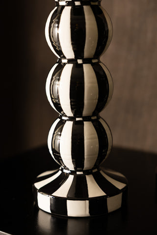 A detailed image of the tall black and white striped candle holder, styled on a dark surface with a smaller version in shot