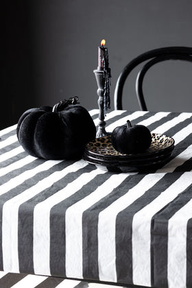 The Black & White Striped Tablecloth styled with plates, black pumpkins and a candlestick holder with melted wax dripping from the lit candle.