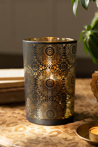 The Black & Gold Lace Pattern Glass Lantern shown styled on a leopard etched wood surface. 