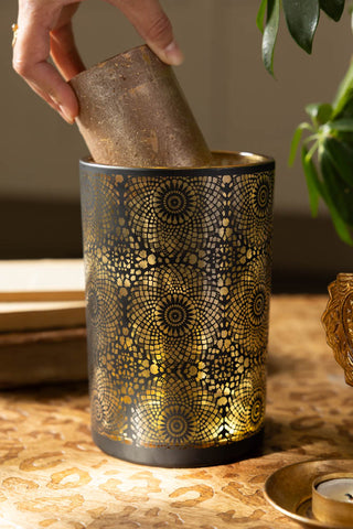 The Black & Gold Lace Pattern Glass Lantern shown with a gold pillar candle being placed inside. 