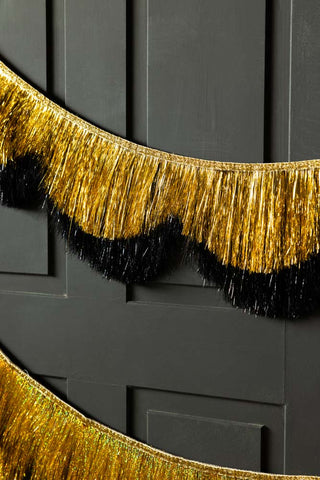 The Black & Gold Scalloped Tinsel Garland styled on a black panelled wall.