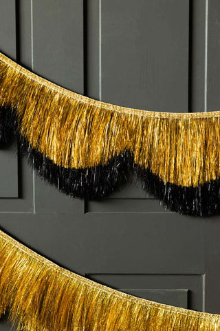 The Black & Gold Scalloped Tinsel Garland styled on a dark wall.