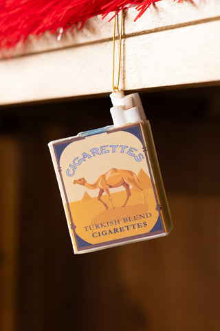 The Blue Cigarette Pack Christmas Tree Decoration displayed hanging from a shelf.