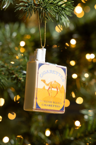 The Blue Cigarette Pack Christmas Tree Decoration displayed hanging ftom a Christmas tree with some fairy lights.