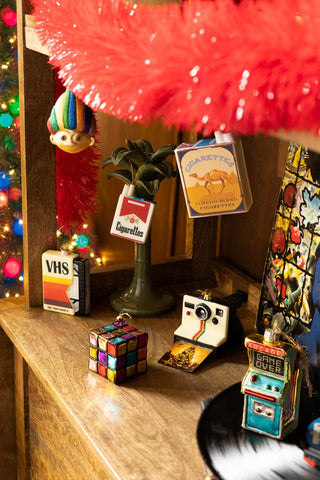 The Blue Cigarette Pack Christmas Tree Decoration styled with various other decorations on a wooden sideboard.
