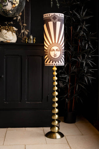 The Solar Goddess Bobbin Floor Lamp in front of a black sideboard and plant.