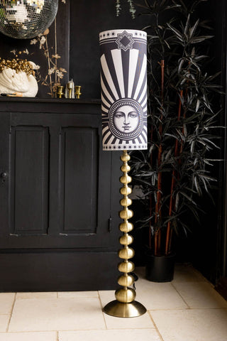 The Solar Goddess Bobbin Floor Lamp in the corner of a room in front of some black furniture.