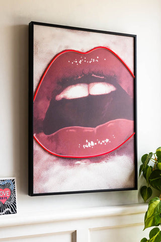 The Bold Red Lip Neon Wall Art styled on a white wall with a plant in the background. 