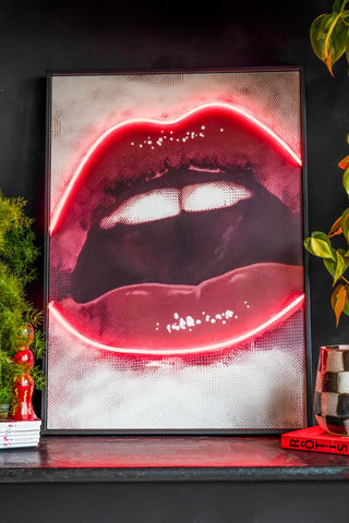 A head on shot of the Bold Red Lip Neon Wall Art styled against a black wall with plants. 