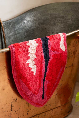 Red lip-shaped bath mat draped over a metal bath.