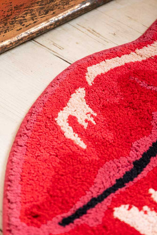 Detail shot of a red lips bath mat displayed on a wooden floor.