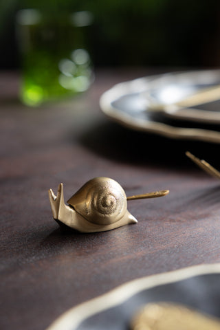 The Brass Disco Snail Salt Cellar displayed on a table amongst some dinner plates and cutlery.