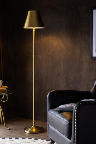 The Brass Slim Floor Lamp switched on and styled next to an armchair and side table.