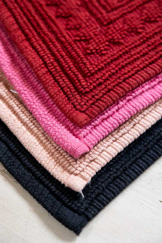 The corner of the Filthy Animal Cherry Red Bath Mat, shown against the other colours in the collection. 