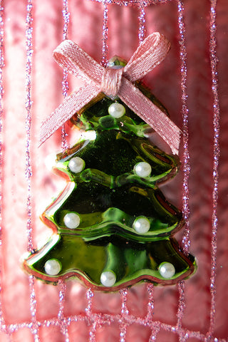 Green Christmas tree ornament with white beads and a pink bow on a pink background