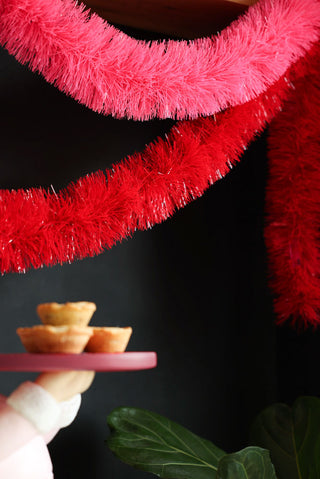 The Bright Red Tinsel displayed draped with some Christmas accessories and a plant.