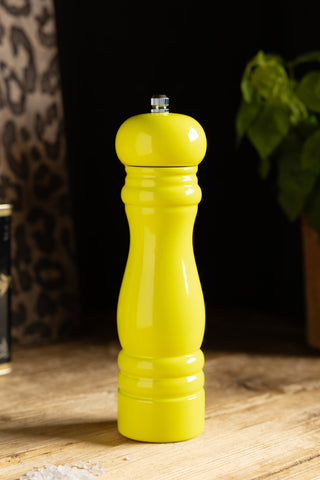 The Neon Yellow Salt/Pepper Mill displayed on a wooden surface with a plant and some accessories in the background.