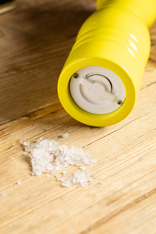 The Neon Yellow Salt/Pepper Mill laying on its side next to some salt, displayed on a wooden surface.