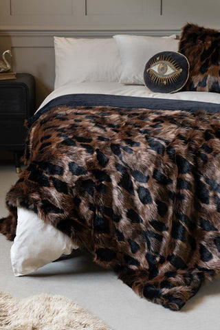 The Chocolate Abstract Faux Fur Throw shown on a bed with neutral bedlinen and panelled walls. The colours on the throw include rich brown and blacks. 