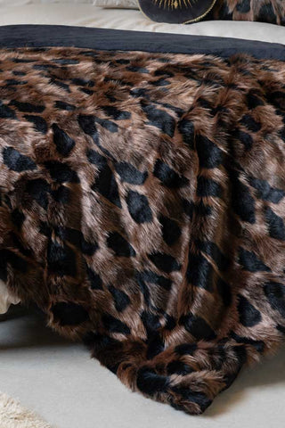 The Chocolate Abstract Faux Fur Throw shown on the edge of a bed. 
