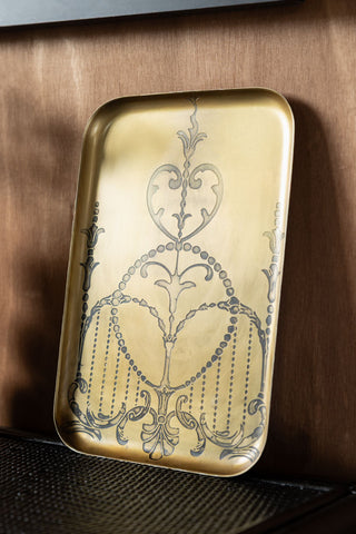 The Brushed Gold Art Nouveau Tray displayed leaning against a wooden wall.