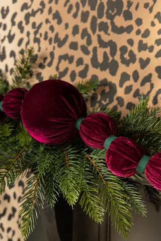 The Burgundy Velvet Sphere Christmas Garland styled with some greenery in front of a leopard print background.