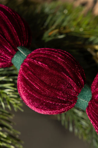 Close-up of the Burgundy Velvet Sphere Christmas Garland with some greenery behind it.