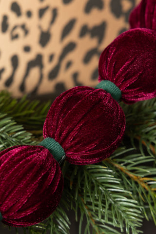 Close-up of the Burgundy Velvet Sphere Christmas Garland with some greenery and  leopard print in the background.
