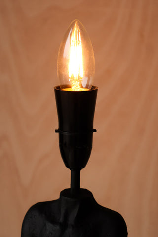 Lifestyle image of the Candle B22 4W Clear LED Light Bulb on a black lamp which is switched on. 