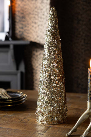 The Champagne Gold Sequin Christmas Tree Cone shown on a wood dining table. 