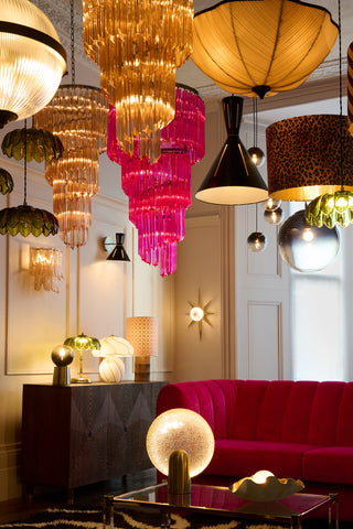 Beautiful portrait image of stunning glass chandeliers, cone ceiling lights suspended from the ceiling with table lamps styled on coffee tables and sideboards.