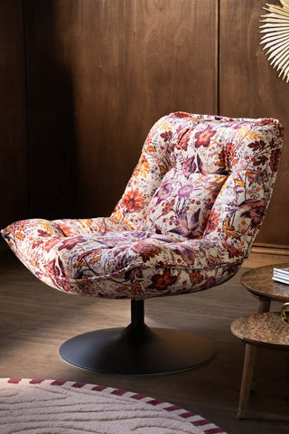 The Charleston Garden Floral Velvet Swivel Chair shown against a dark wood textured wall. 