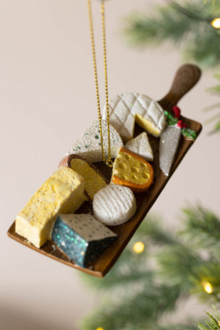 The Cheese Board Christmas Decoration  shown with a Christmas tree in the background. 