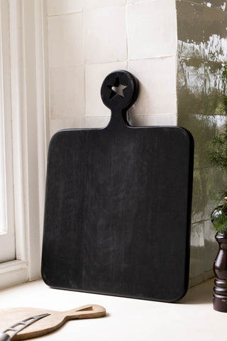 The back of the Cheese Slut Square Wooden Serving Board shown in a kitchen against white zellige tiles. 
