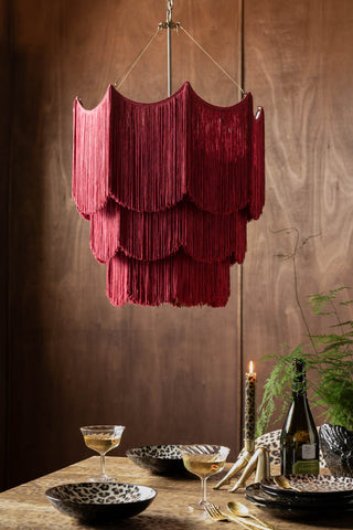 Cherry Red Tiered Fringe Chandelier shown against a textured wood wall above a dining table with leopard print plates. 