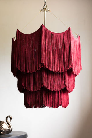 The Cherry Red Tiered Fringe Chandelier shown against a white wall. 